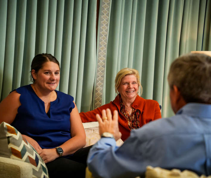 A man talking to two women sitting on a couch.